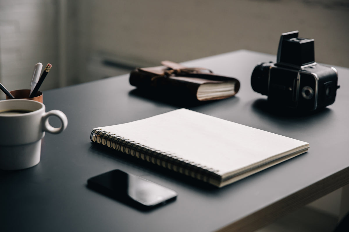 Blank notebook on a desk with camera and coffee cup